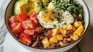 Un bol contenant des aliments, notamment de l’avocat, des tomates et un œuf poché.