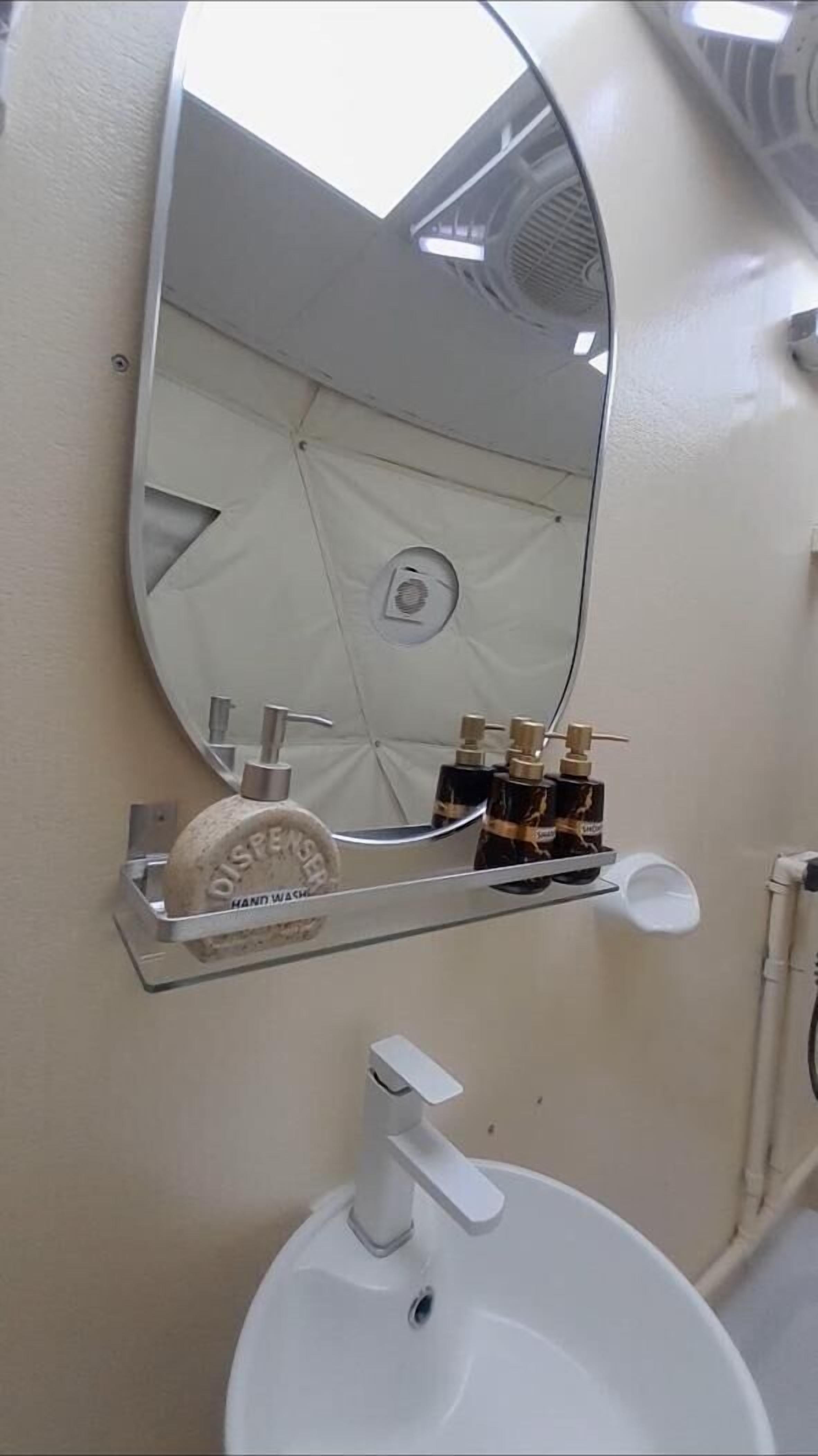 A bathroom with a white sink, a mirror, and a soap dispenser.