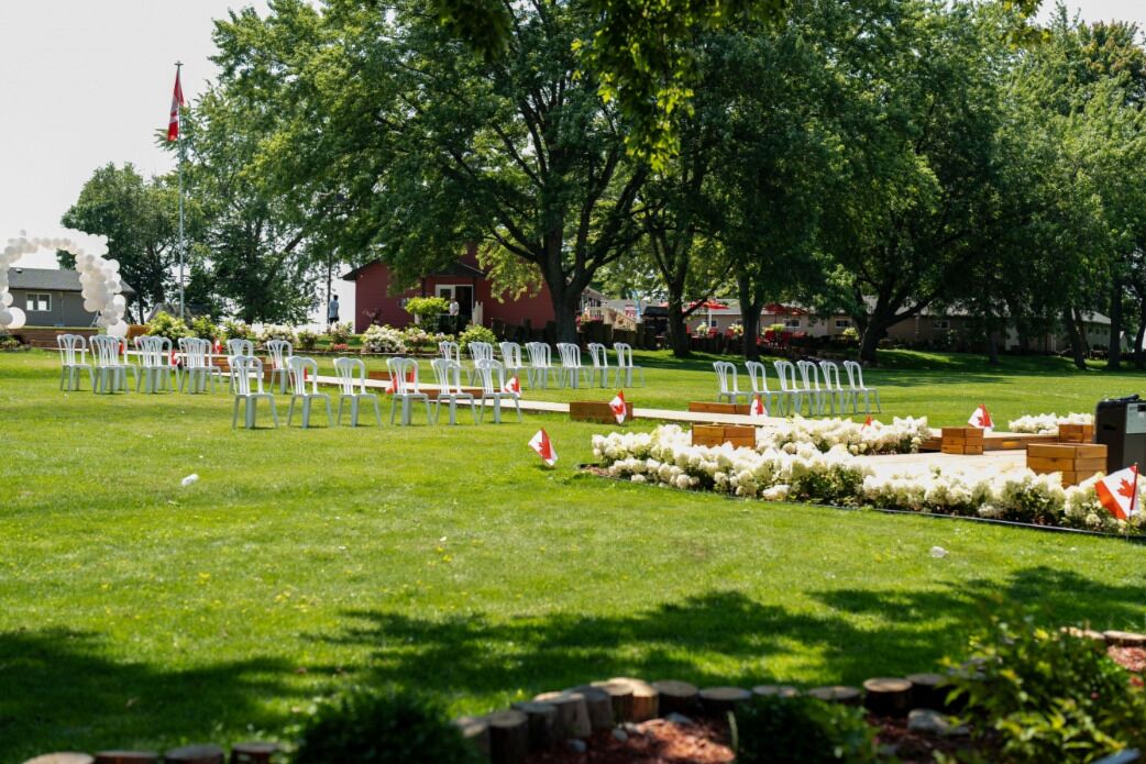 An outdoor seating area with white chairs arranged in rows, a flag, and a small building in the background.
