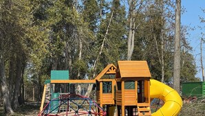 Une structure de jeux en bois, avec un toboggan et des éléments d’escalade, installée dans un parc.