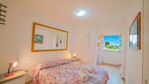 Een slaapkamer met een bed, nachtkastje, lamp en een raam met uitzicht.