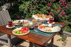 Una mesa al aire libre con diversas comidas y bebidas, rodeada de follaje y flores.