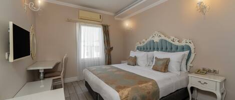 A hotel room with a bed, bedside table, chair, desk, and a TV.