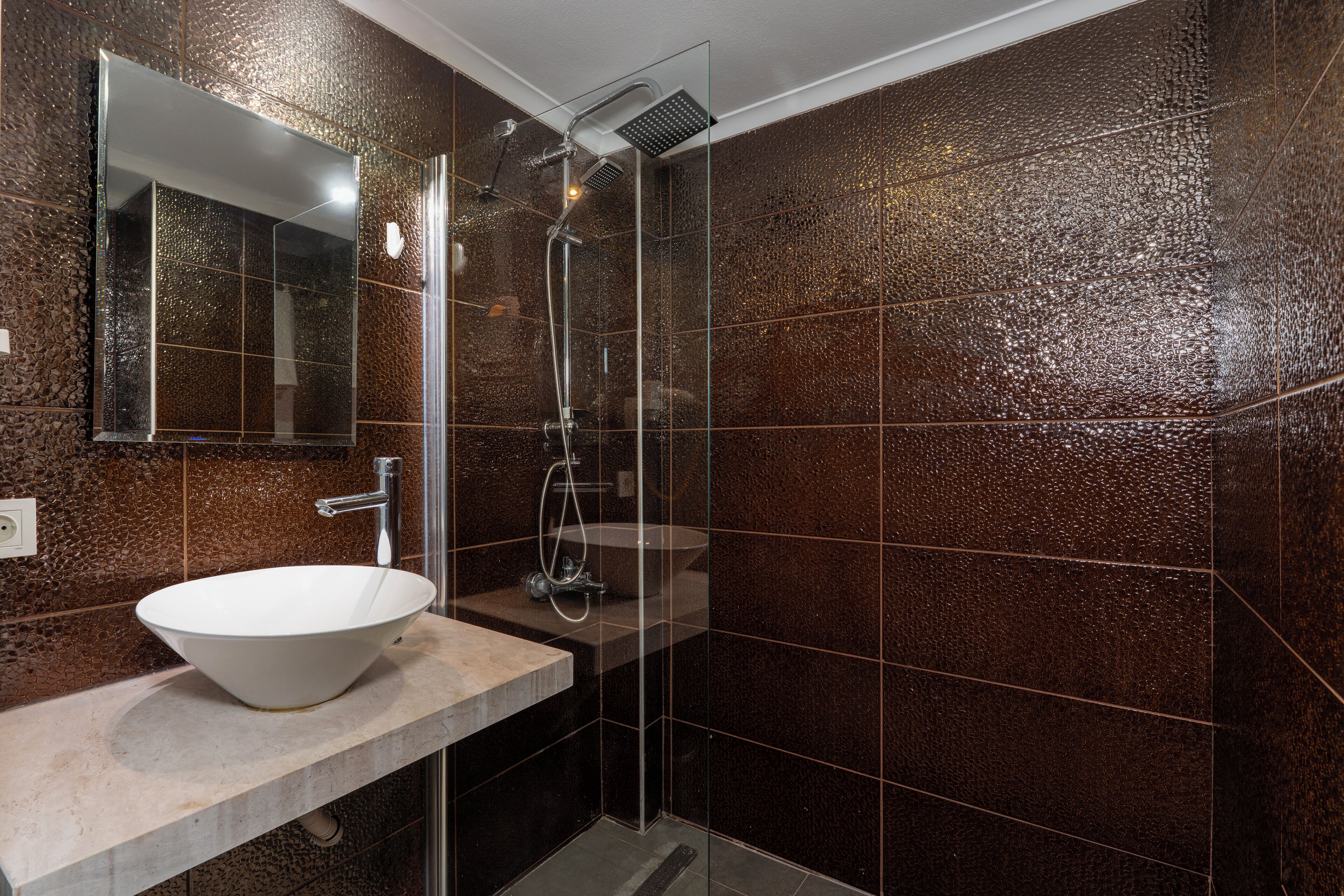 A modern bathroom with a large mirror, a white vessel sink, and a glass-enclosed shower area.