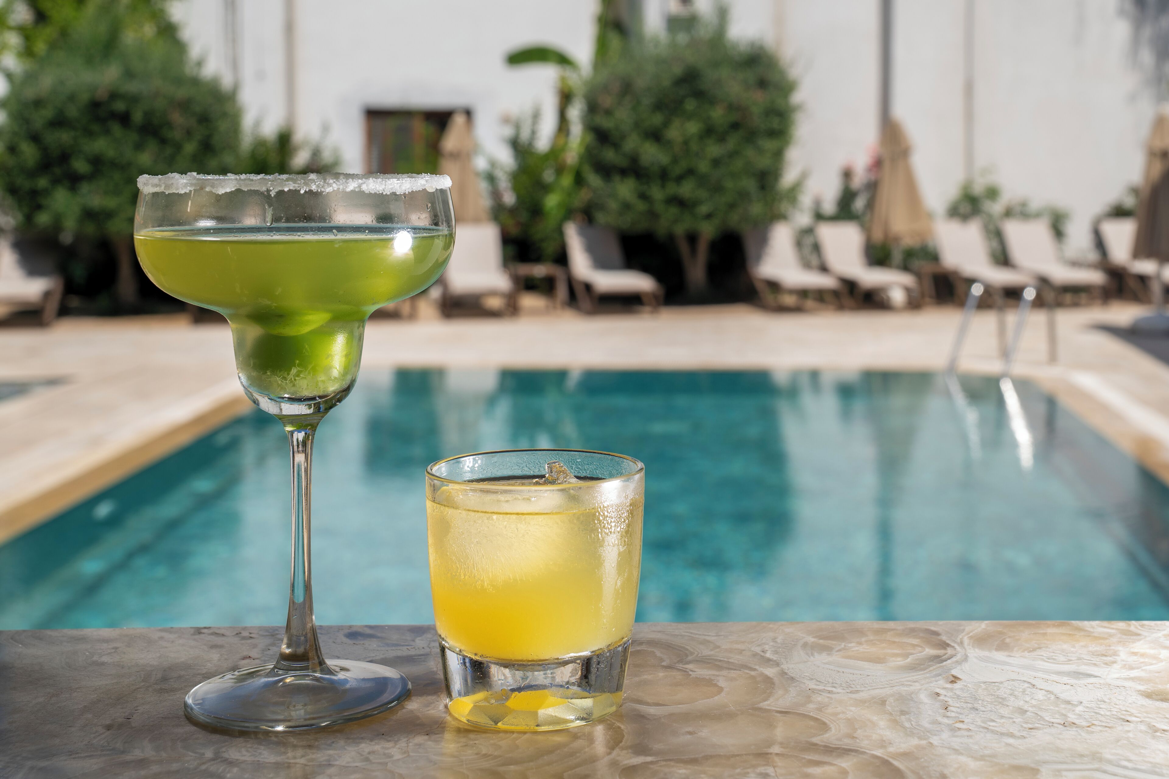 A cocktail glass and a shot glass with a green drink by a poolside.