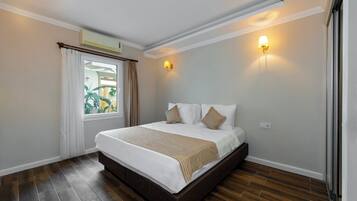 Un lit bien fait, recouvert d’une couverture rayée blanche et beige, une fenêtre avec des rideaux et un luminaire fixé au mur.