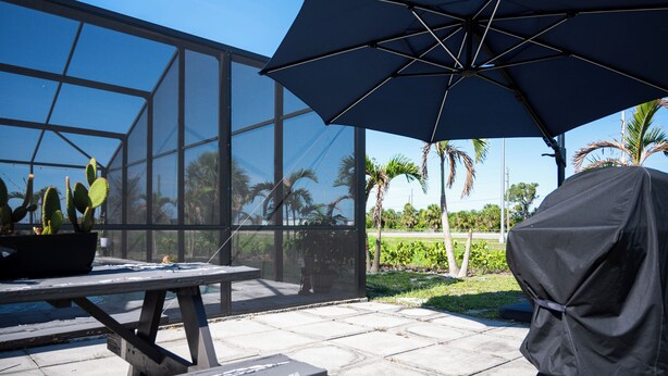 Un espace patio doté d’une véranda en verre, d’une table ornée d’une plante en pot et d’un grand parasol.
