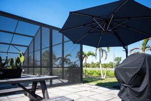 Un patio con cerramiento de vidrio, una mesa con una planta en maceta y un paraguas grande.