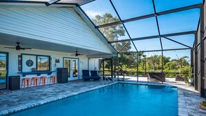 Une piscine avec un patio couvert, un espace salon extérieur et une vue sur la végétation environnante.