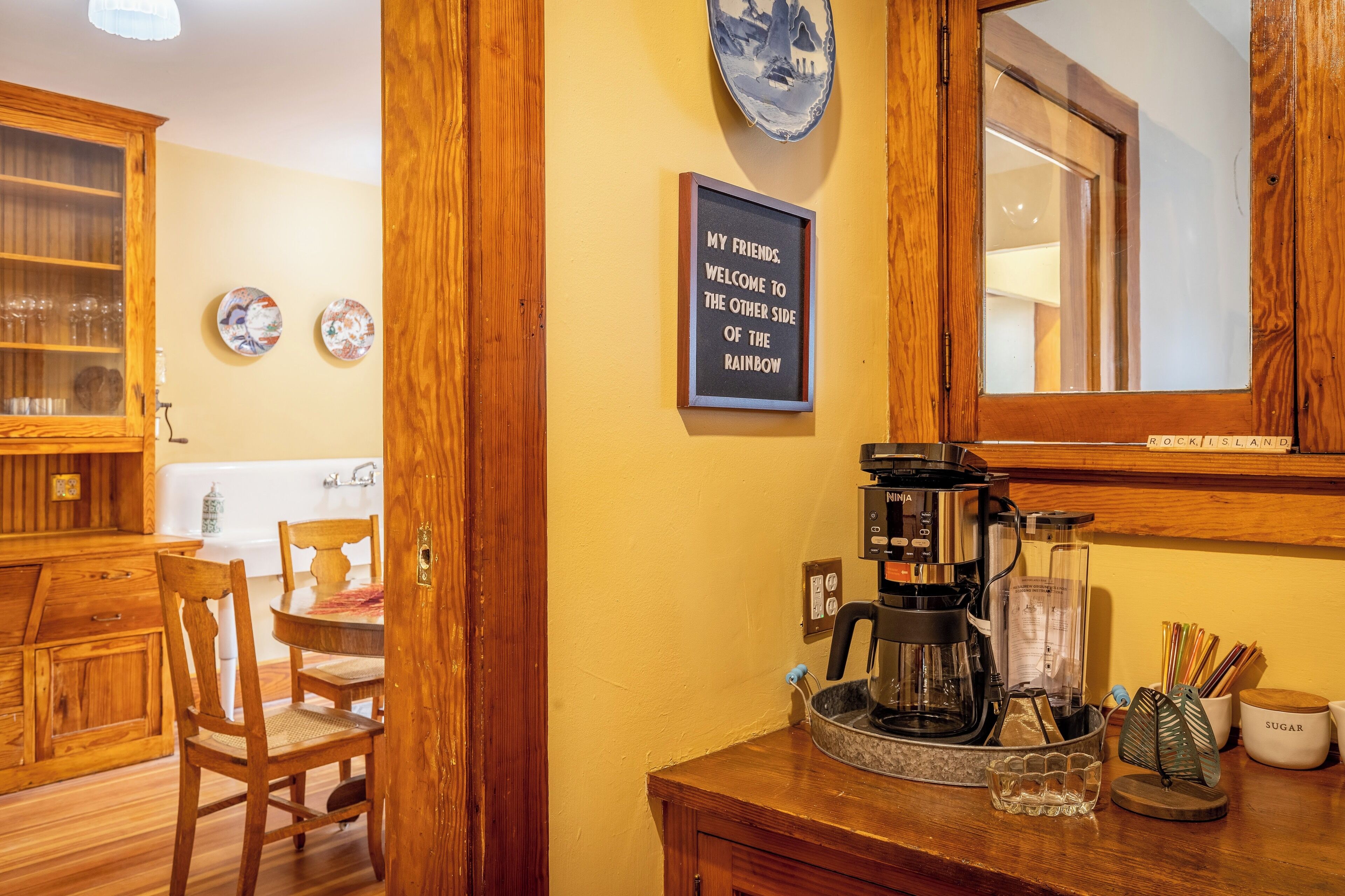 A wooden interior with a coffee maker, a framed welcome sign, and a dining area.