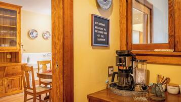 A wooden interior with a coffee maker, a framed welcome sign, and a dining area.
