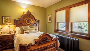Ein Schlafzimmer mit einem hölzernen Bett, einem Nachttisch, einer Lampe, einem Heizkörper und einem Fenster mit Jalousien.