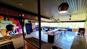 A modern kitchen with a central island, a dining area with chairs, and a colorful mural on the wall. - CoCo Bongo Hostel (Bahia de Caraquez)
