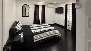 A modern bedroom with a bed, a mirror, an air conditioning unit, a TV, and a thermostat.