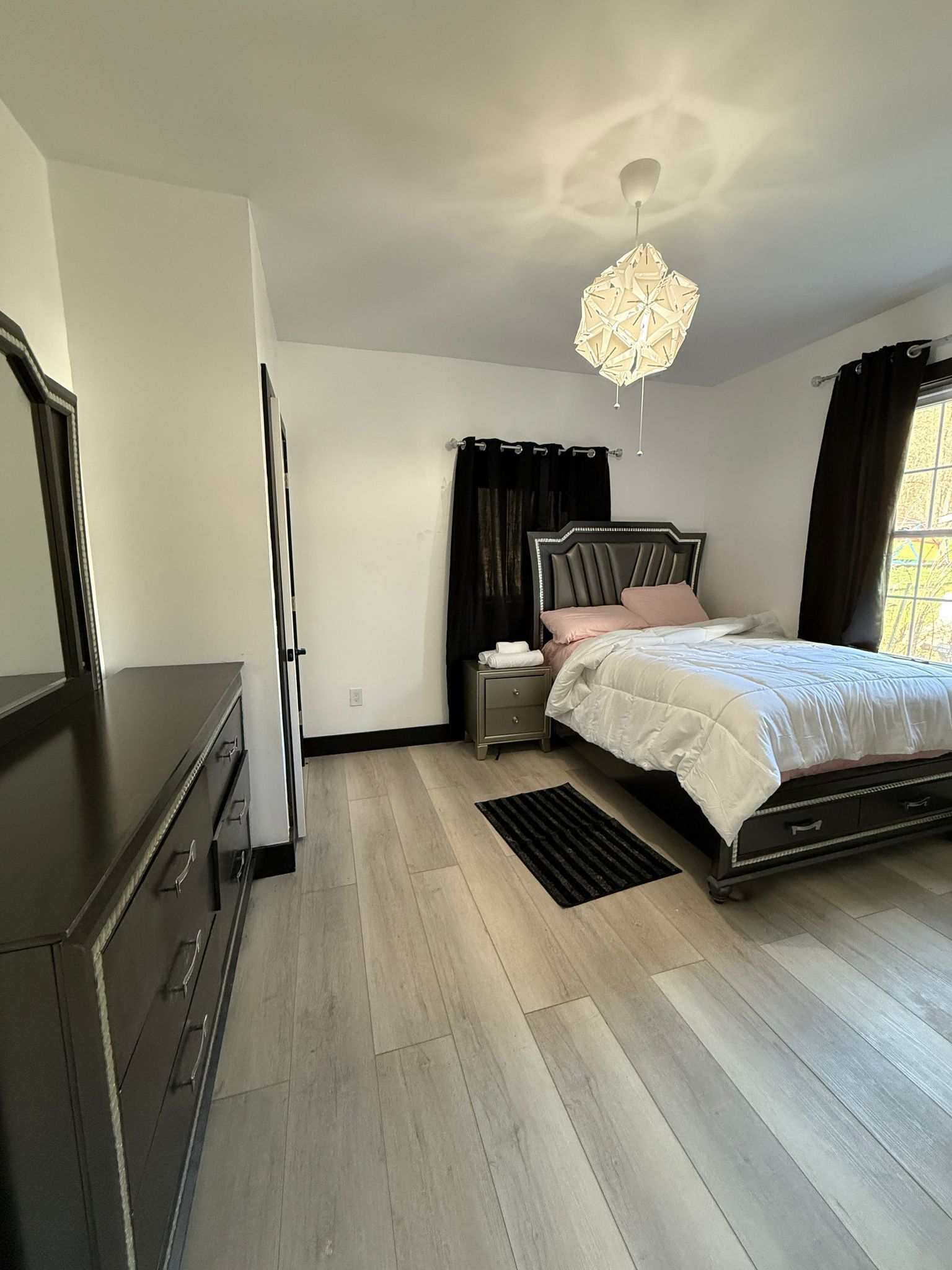 Een slaapkamer met een bed, nachtkastje, kaptafel en een plafondlamp.