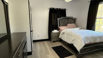 Een slaapkamer met een bed, nachtkastje, kaptafel en een plafondlamp.