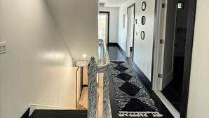 A modern hallway with a black and white patterned carpet, a staircase with a granite handrail, and a door with a black frame.