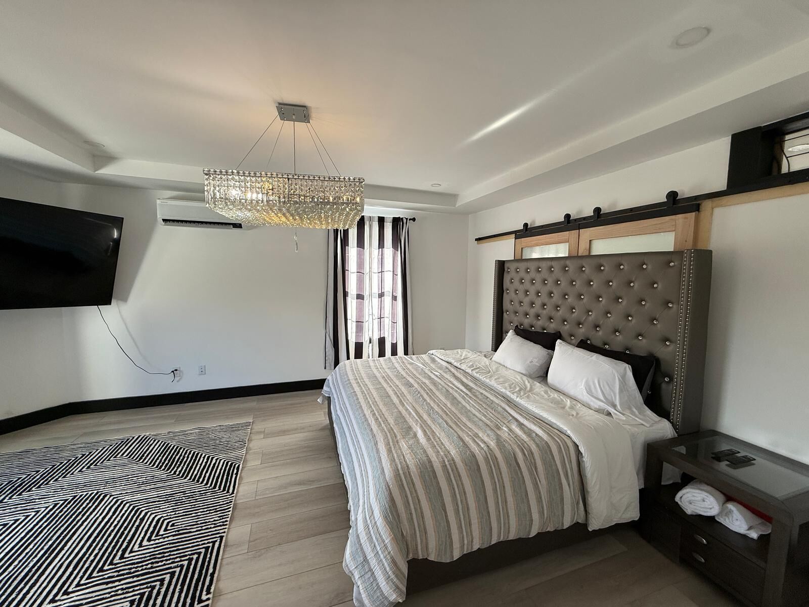 A modern bedroom with a large bed, a television mounted on the wall, and a chandelier.