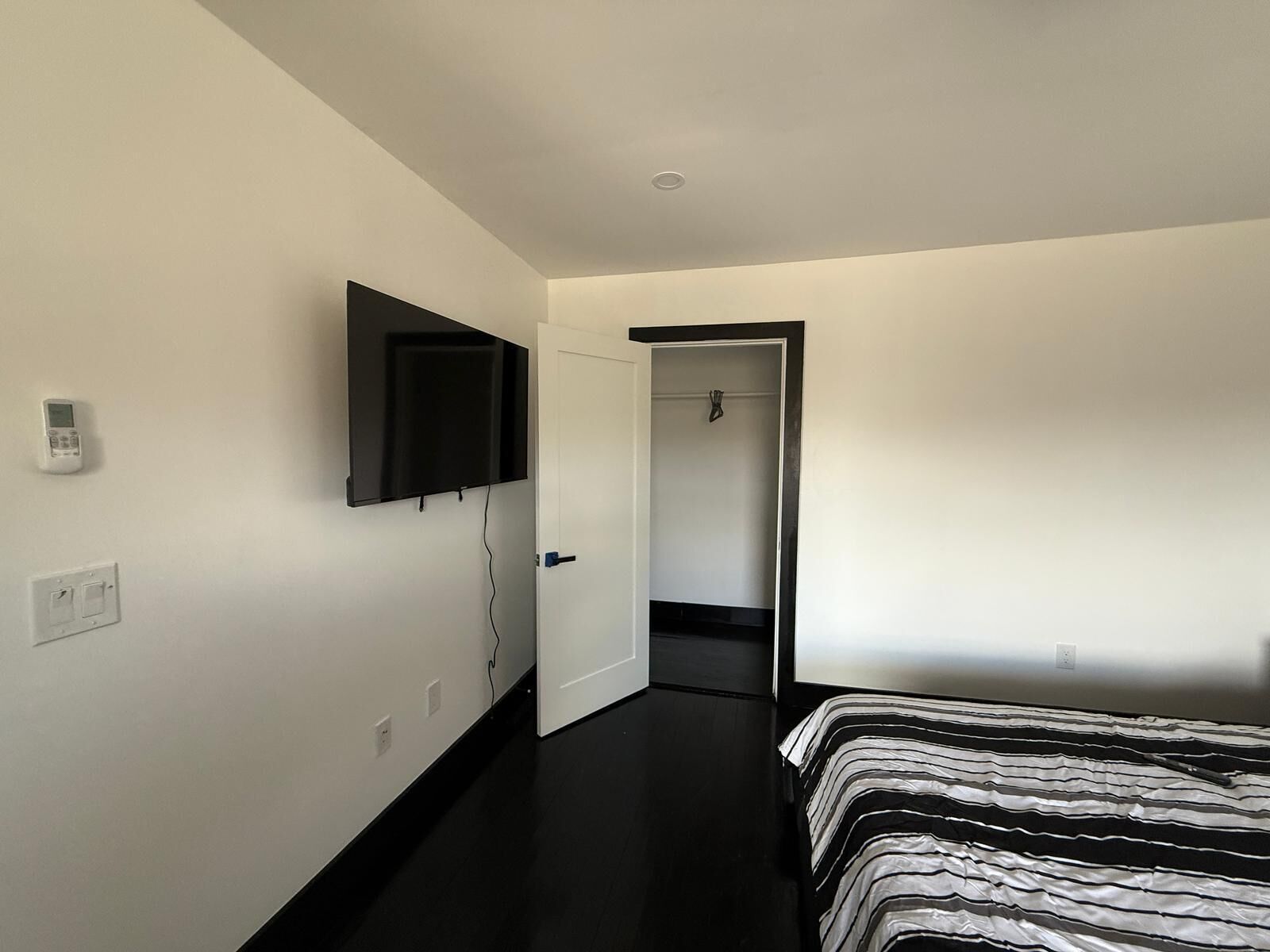A modern bedroom with a large bed, a mounted TV, and a door leading to a bathroom.