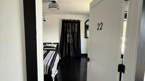 A hallway leading to a bedroom with a bed, a window with curtains, and a door marked with the number 22.