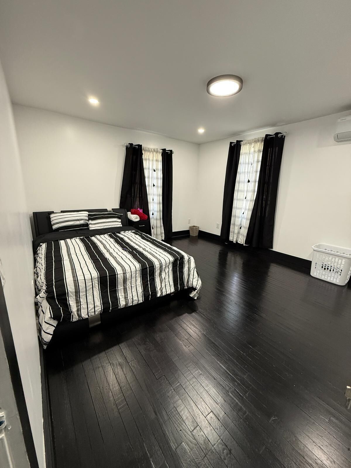 Una camera da letto con un letto grande, pavimento in legno scuro, pareti bianche e tende nere.