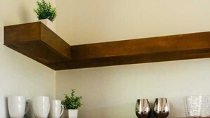 A kitchen with two wooden shelves, a black countertop, and various kitchen items including cups, a kettle, and a plant.