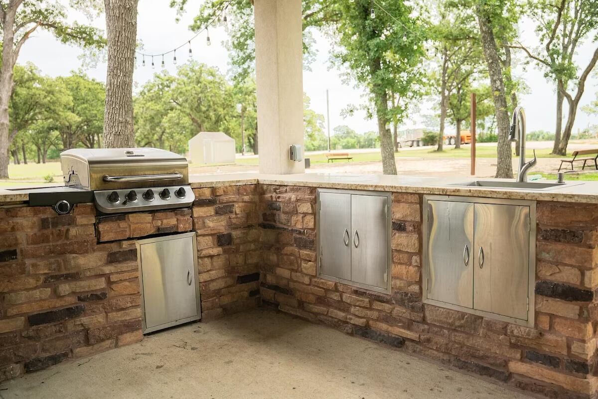An outdoor kitchen with a stone backsplash, a built-in grill, and stainless steel cabinets.