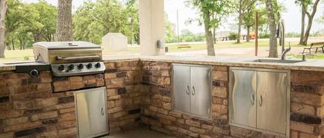 An outdoor kitchen with a stone backsplash, a built-in grill, and stainless steel cabinets.