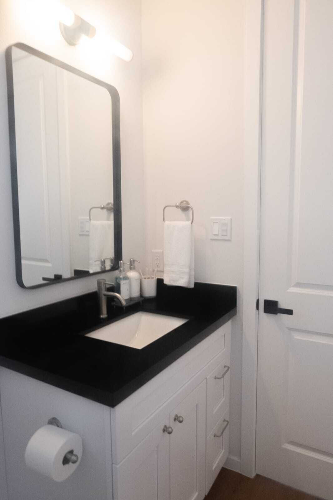 Un baño con lavamanos de encimera negra, espejo, toallero y dispensador de papel higiénico.