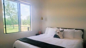 A bedroom with a bed, a nightstand, a lamp, and a window with a view of trees.