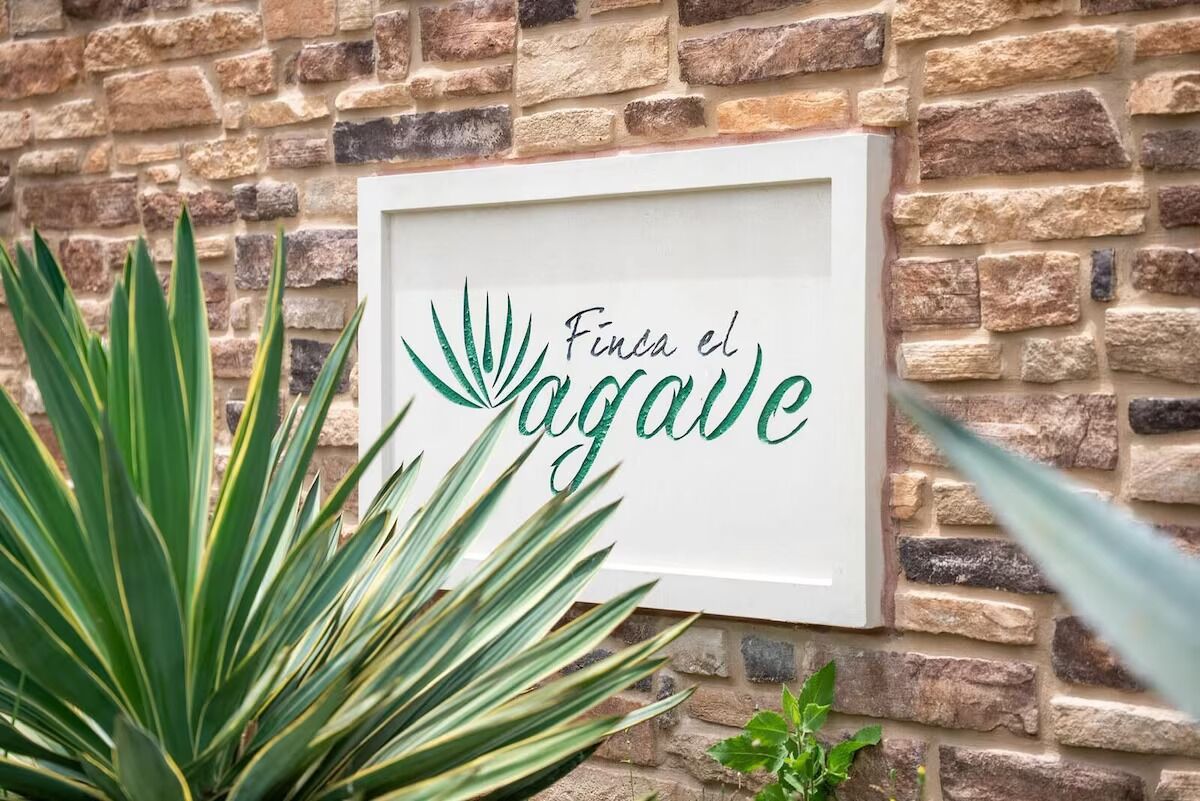 A framed sign with the text "Finca el Agave" on a stone wall.
