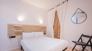 A bedroom with a bed, a wooden headboard, a chair, a mirror, and a window with curtains.