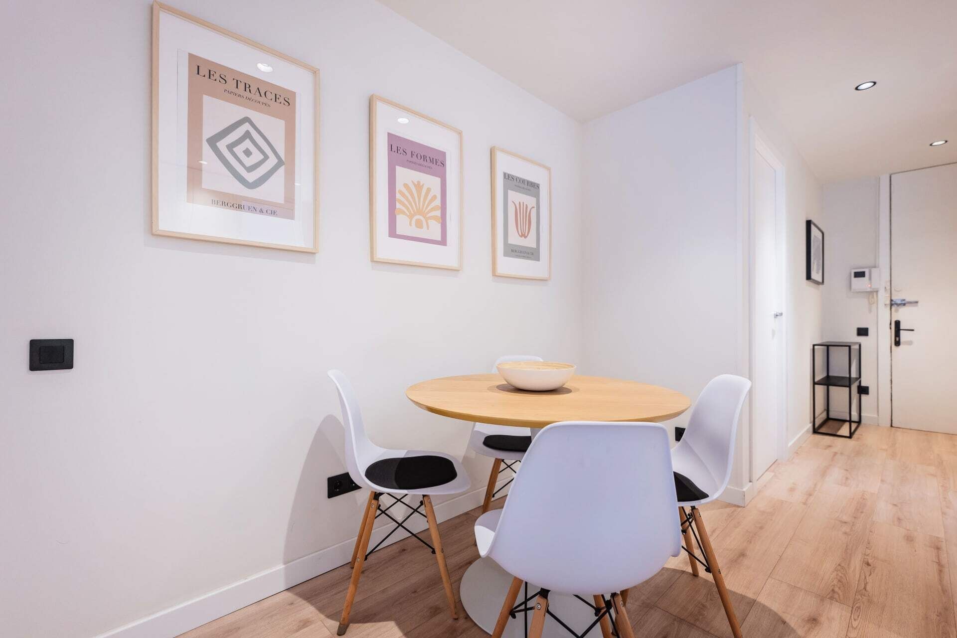 Een eetgedeelte met een ronde tafel, vier witte stoelen en drie ingekaderde kunstwerken aan de muur.