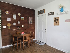 Een eetgedeelte met een houten wand, een witte deur en diverse decoraties, waaronder borden en een vaas.