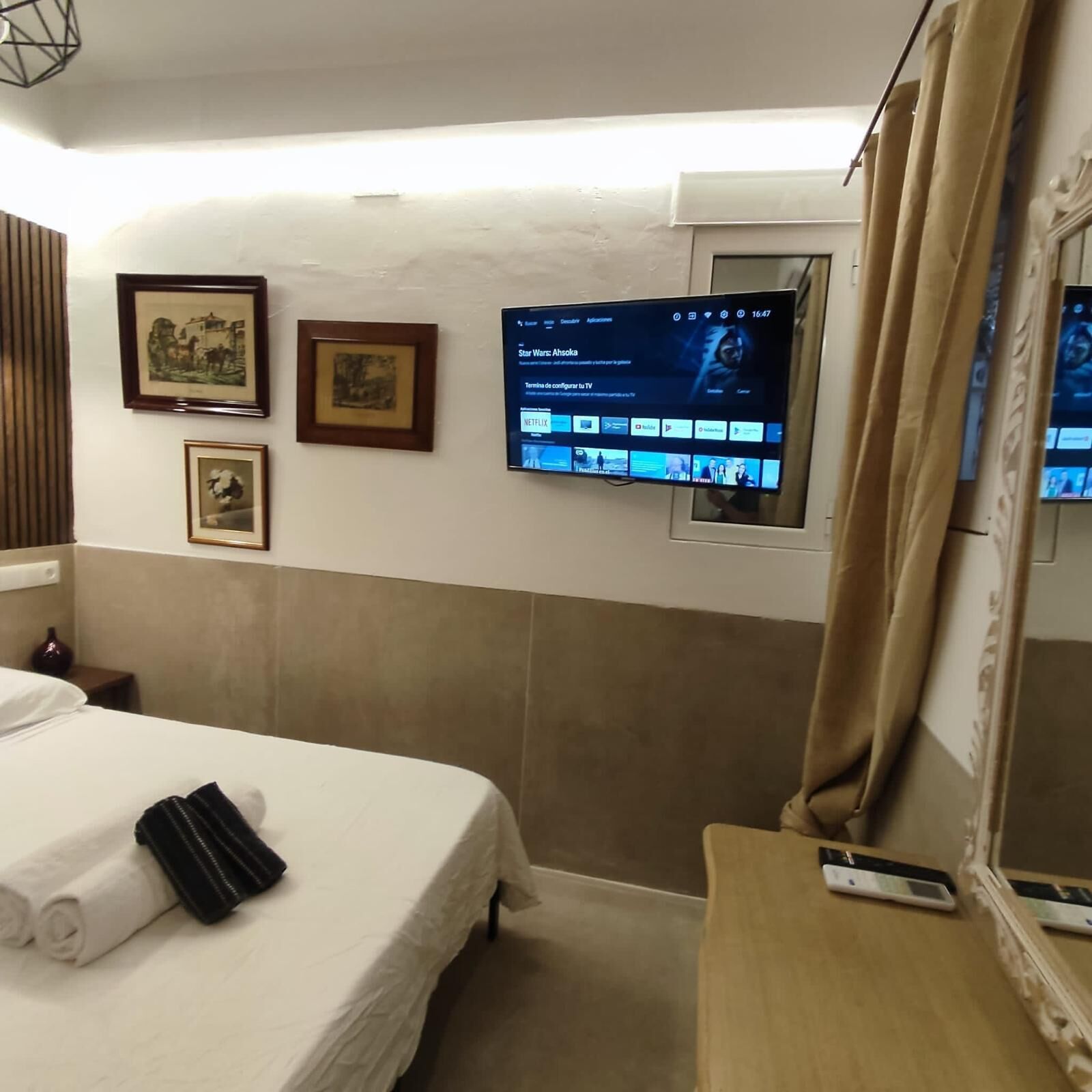 A hotel room with a bed, a TV mounted on the wall, and a mirror on the dresser.