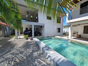 A modern two-story house with a swimming pool, a covered carport, and a balcony with plants. - AJ House & Suites (Bahía Ballena)