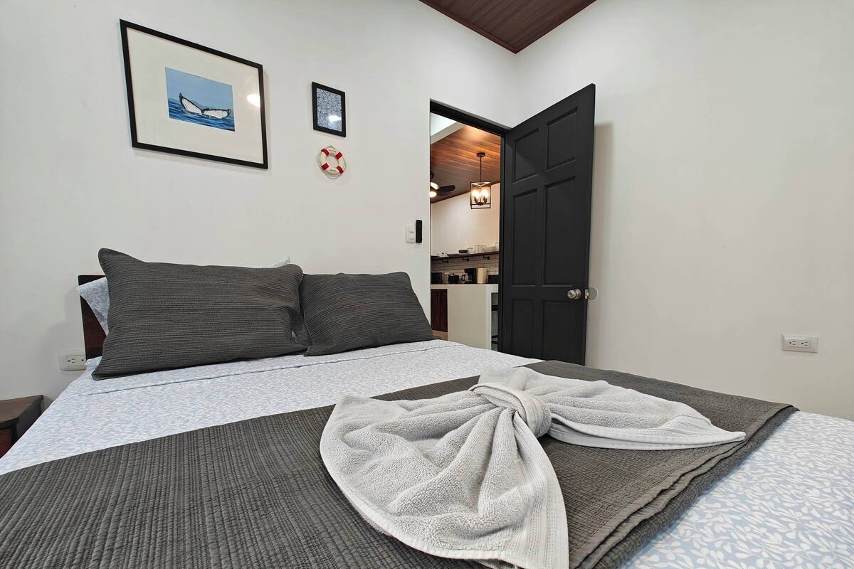 A neatly made bed with a patterned bedspread, two dark pillows, and a towel on the bed.