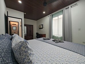 A bedroom with a large bed, a wardrobe, a desk, and a window with curtains. - AJ House & Suites (Bahía Ballena)