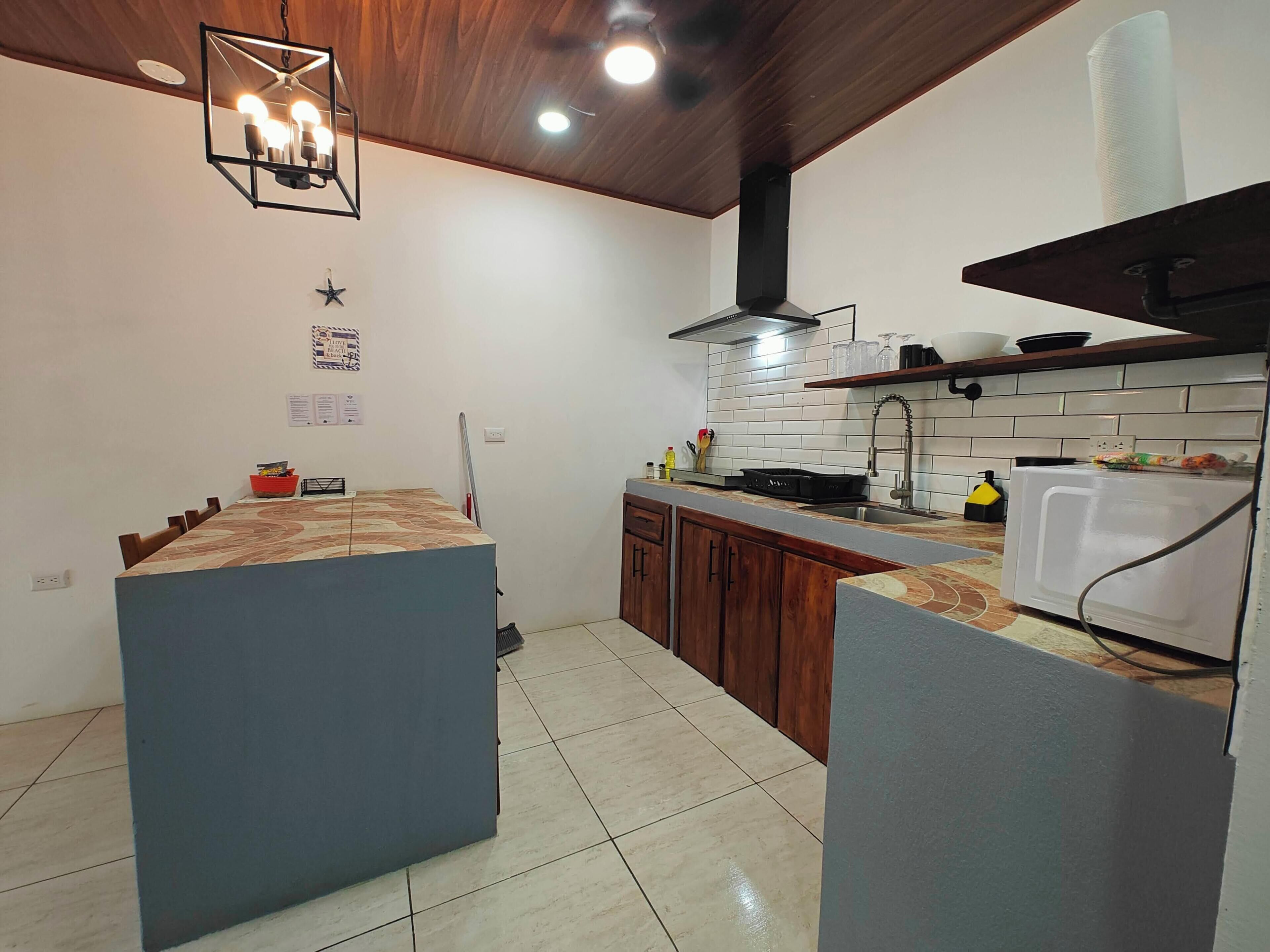 Una cocina con una isla central, armarios de madera, salpicadero de azulejos y una lámpara colgante moderna.