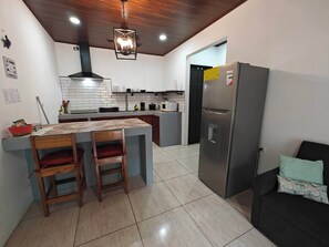 A modern kitchen with a central island, stainless steel appliances, and a wooden ceiling. - AJ House & Suites (Bahía Ballena)