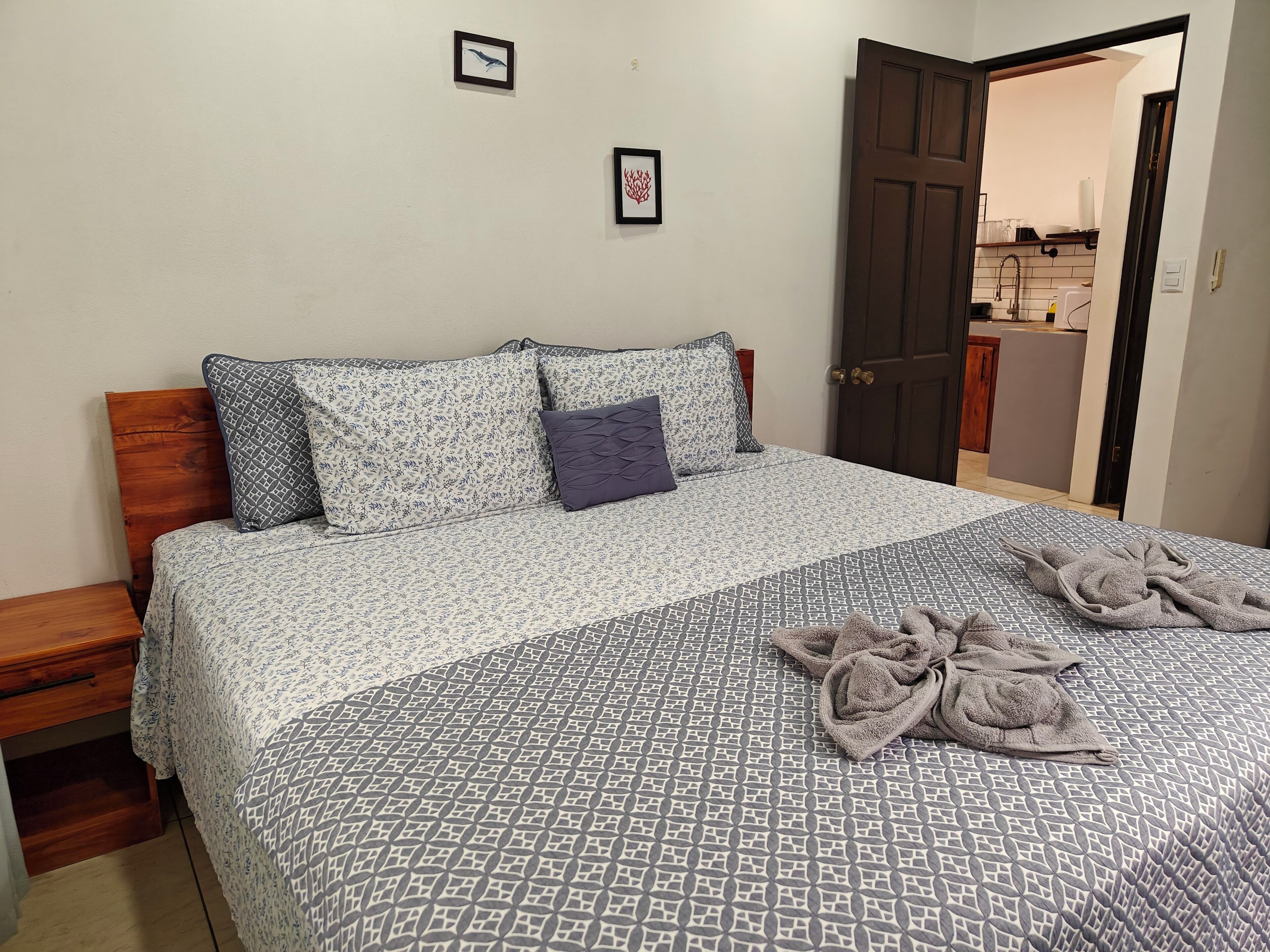 A neatly made bed with patterned bedding, a wooden headboard, and a door leading to a kitchen area.