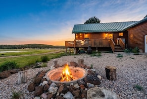 Une cabane avec un foyer au premier plan, entourée de gravier et de rochers.