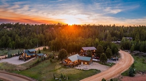 Un chalet doté de plusieurs cabanes, un chemin de terre et un paysage boisé en arrière-plan.