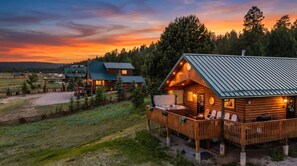 Eine Blockhütte mit einer Terrasse und Sitzgelegenheiten im Freien, umgeben von einem eingezäunten Grundstück und Bäumen.