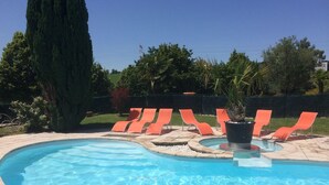 Une piscine à bord incurvé, entourée de chaises longues orange et agrémentée d’une plante en pot.