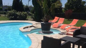A swimming pool with a stone deck, surrounded by orange lounge chairs and a black wicker table.