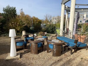 A patio area with outdoor seating, including round tables and chairs, surrounded by gravel. - Balladins Lyon Est (Saint-Quentin-Fallavier)