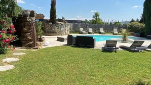 Un jardin avec une piscine, des chaises longues et un mur en pierre.
