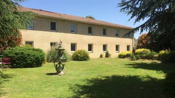 A building with a tiled roof and multiple windows, surrounded by well-maintained grass and shrubs.