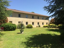 A building with a tiled roof and multiple windows, surrounded by well-maintained grass and shrubs.